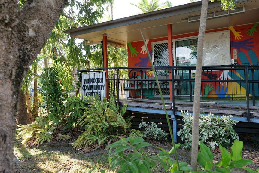 Orange building with colourful hands painted on the walls surrounded by tropical plants with Manoora Community Centre sign