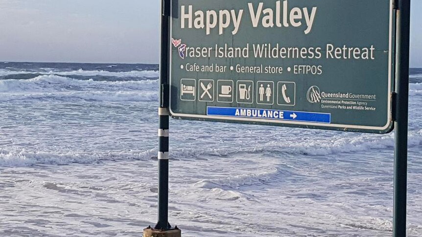 Ocean waves lapping at the foot of a sign on Fraser Island