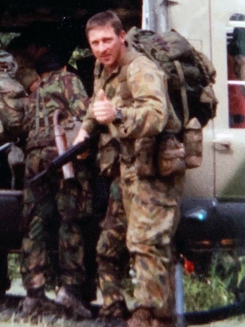 A man in camouflage uniform carrying a machine gun gives a thumbs-up sign as he boards a helicopter.