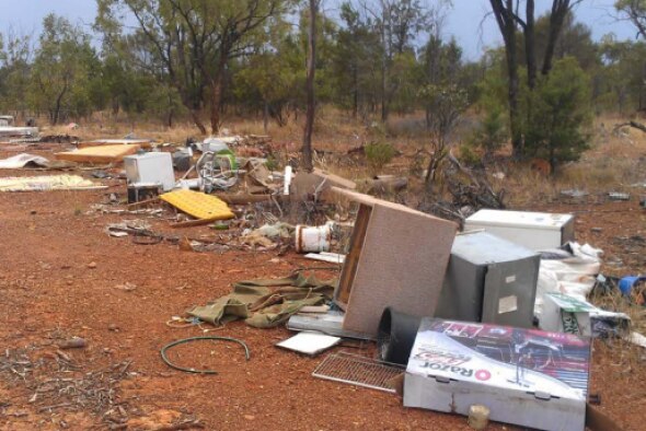 Furniture, whitegoods, electricals and other miscellaneous waste has been dumped on the side of a road girt by red dirt.