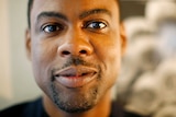 A close-up photo of Chris Rock's face, he's smiling and looking at the camera