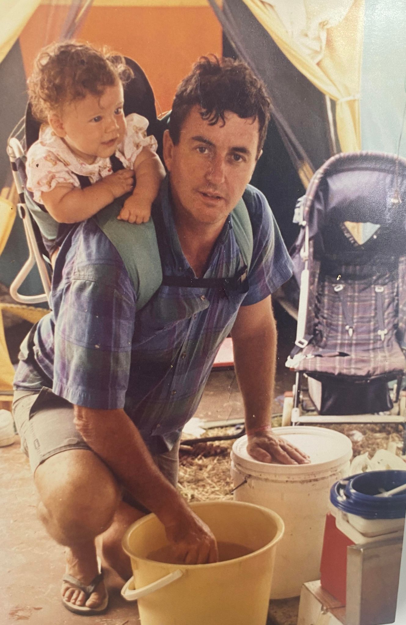 Alan Ballantyne with his daughter on his back and his hands in two buckets, a pram is visible behind