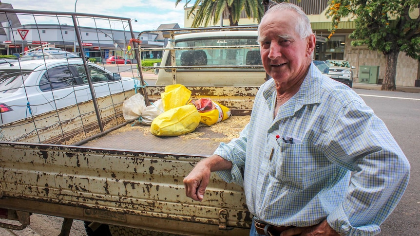 A farmer stands at the back of his truck parked in the street