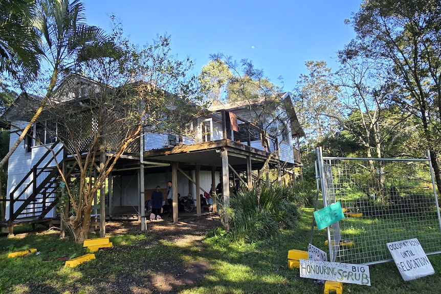 A house on stilts behind a fence with placards leaning against it.