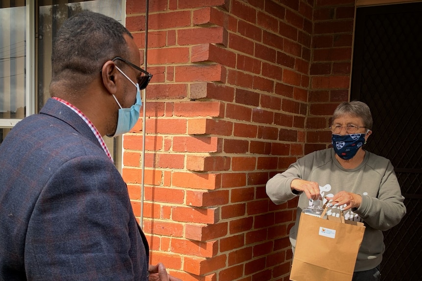 Ahmed Tohow chats to a woman outside the front door of her brick home in Melbourne's suburbs.