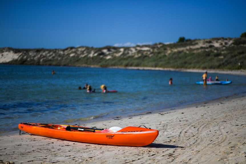 An orange kayak sits on a beach.