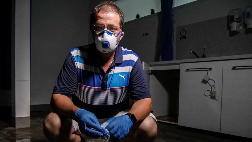 A man looks up at the camera, wearing a face mask, in a flood-affected room.