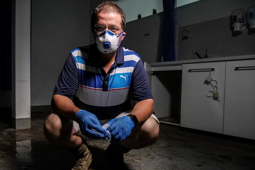 A man looks up at the camera, wearing a face mask, in a flood-affected room.