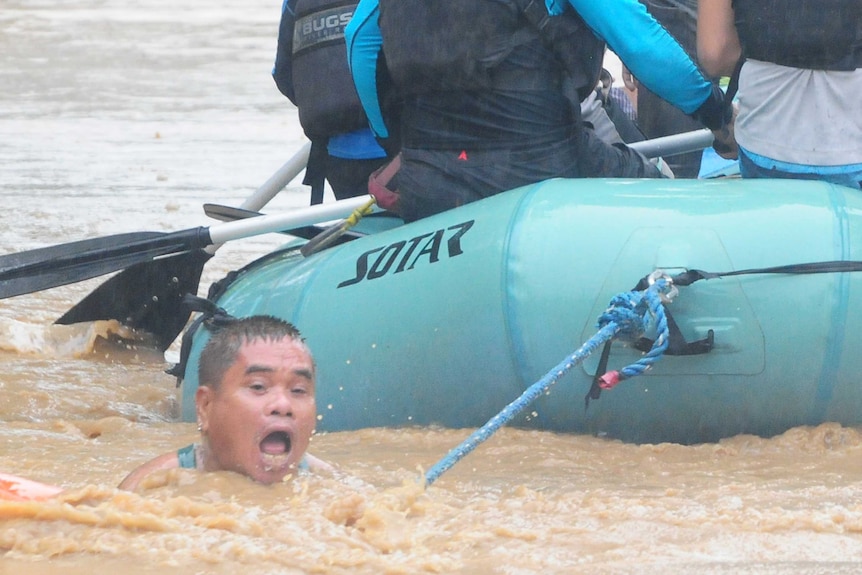 A man clings onto the rope of a rescue boat as residents are evacuated from their homes due to heavy flooding