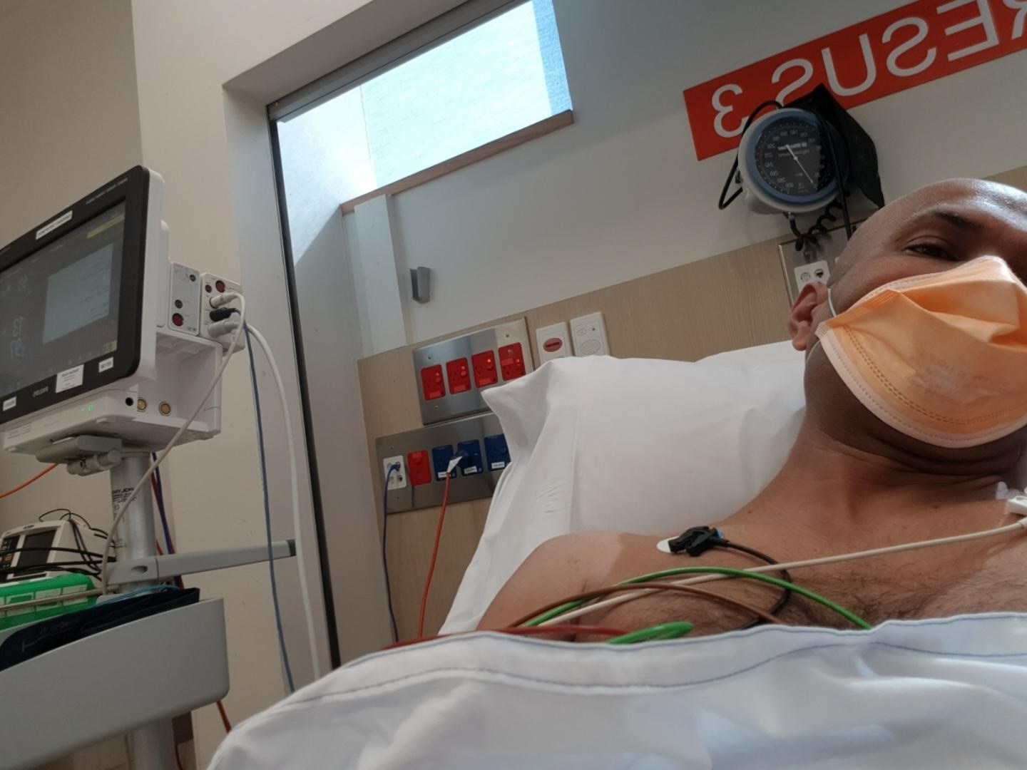 A man in a hopital bed wearing a facemask.