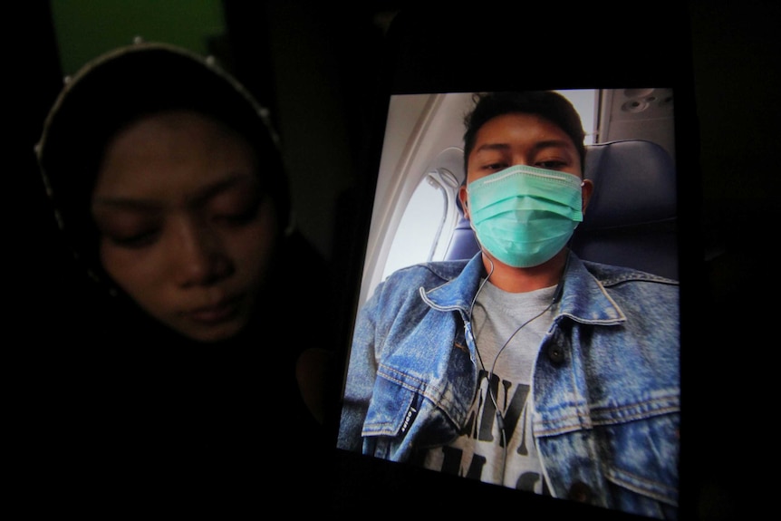 A woman holds up a picture showing her husband on board a plane.