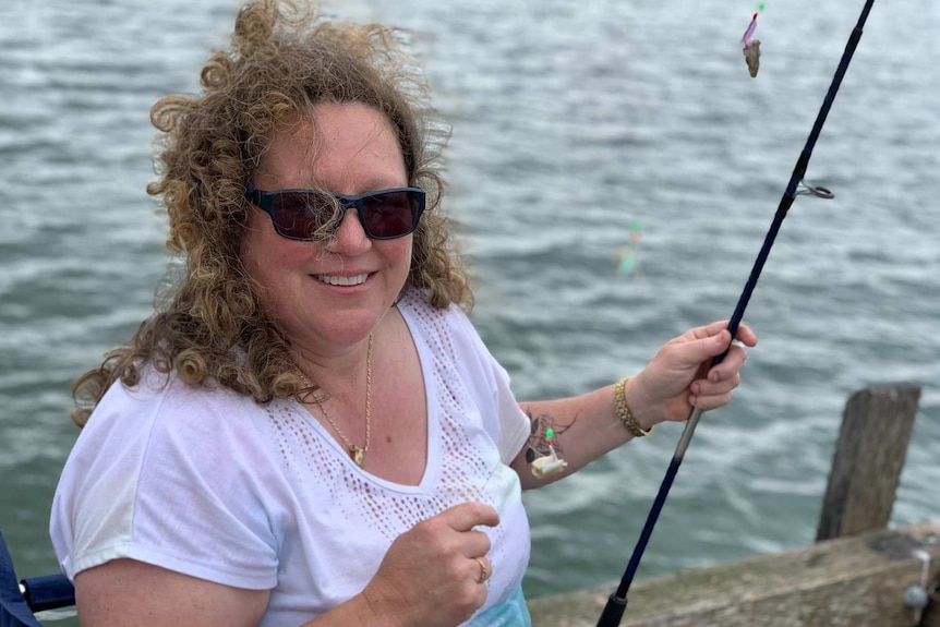 A woman holds a fishing rod and smiles at the camera