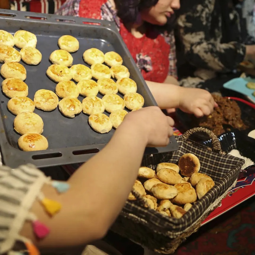 A person holding an oven tray with fresh traditional Iraq cookies and placing them into a basket