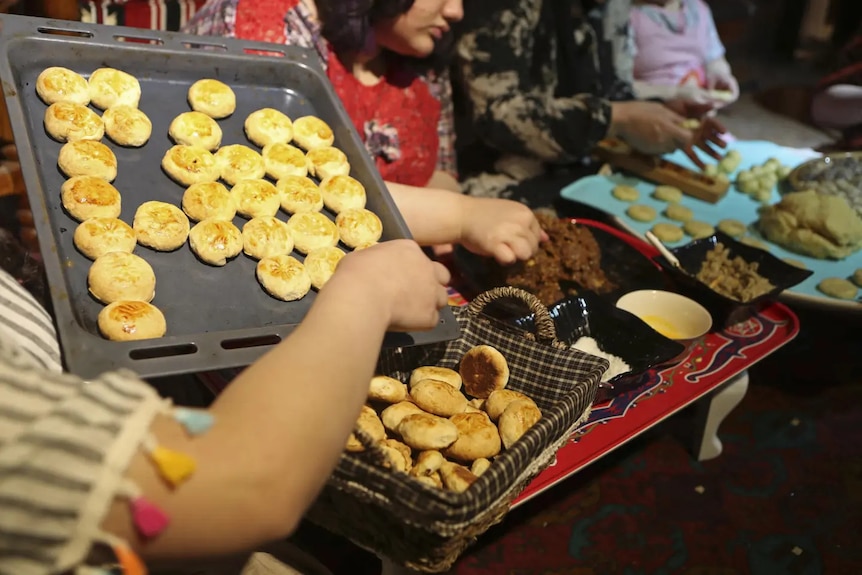 A person holding an oven tray with fresh traditional Iraq cookies and placing them into a basket