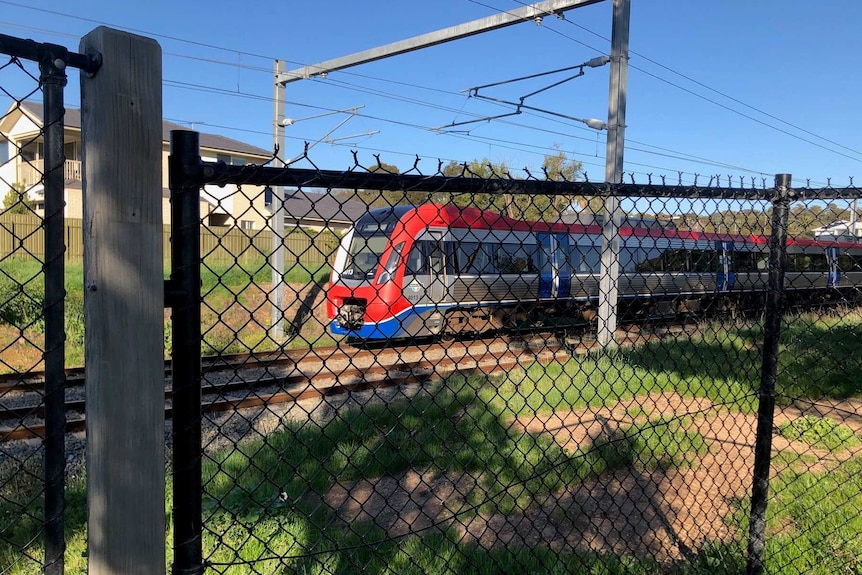 A train travelling on train tracks behind a black wire fence