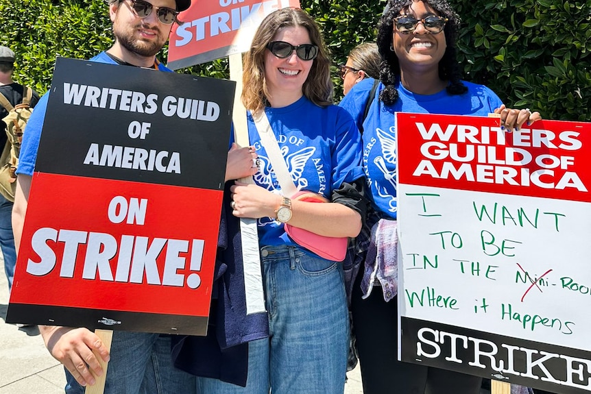 Two women and a man hold up signs with Writers Guld of America and Stirke written on them.