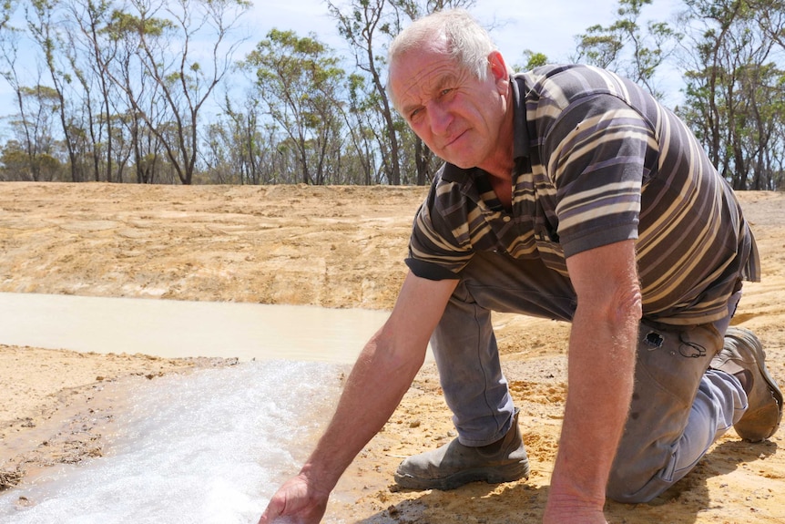 Jerramungup farmer Bill Bailey leans down and puts his hand in a stream of water.