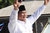 Prabowo Subianto stands out of a car and holds his hands up to the crowd who cheer and take photos.