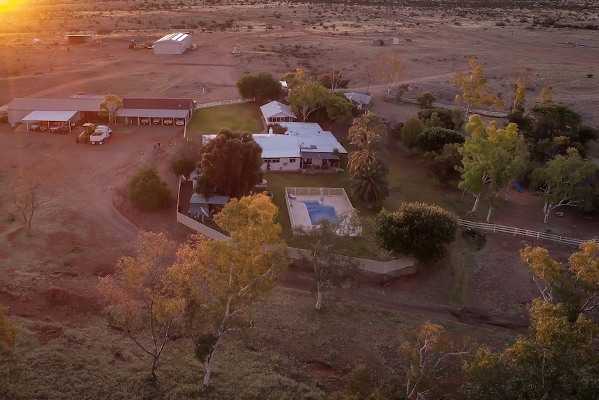 A drone photo of a couple of buildings,  including pool on red soil as sun rises in the horizon.