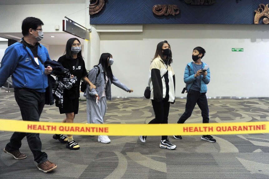 People wearing surgical masks walk past an area roped off with tape that says "quarantine".