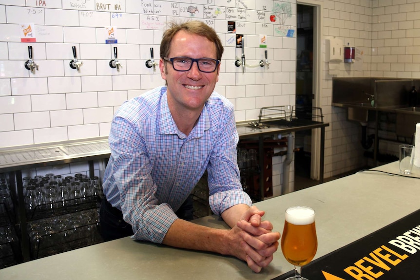 Matt Kirkegaard leaning on a bar with a glass of beer in front of him.