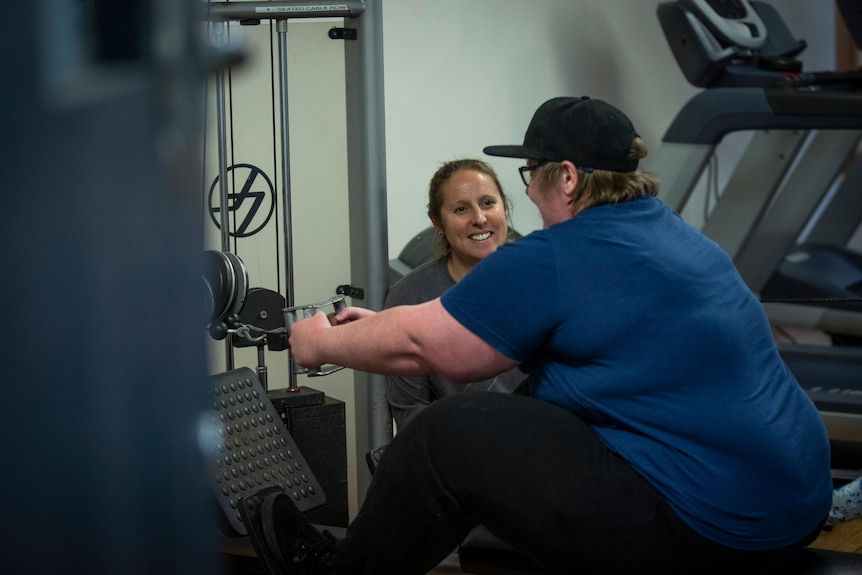 A woman smiling, instructing a gym client.