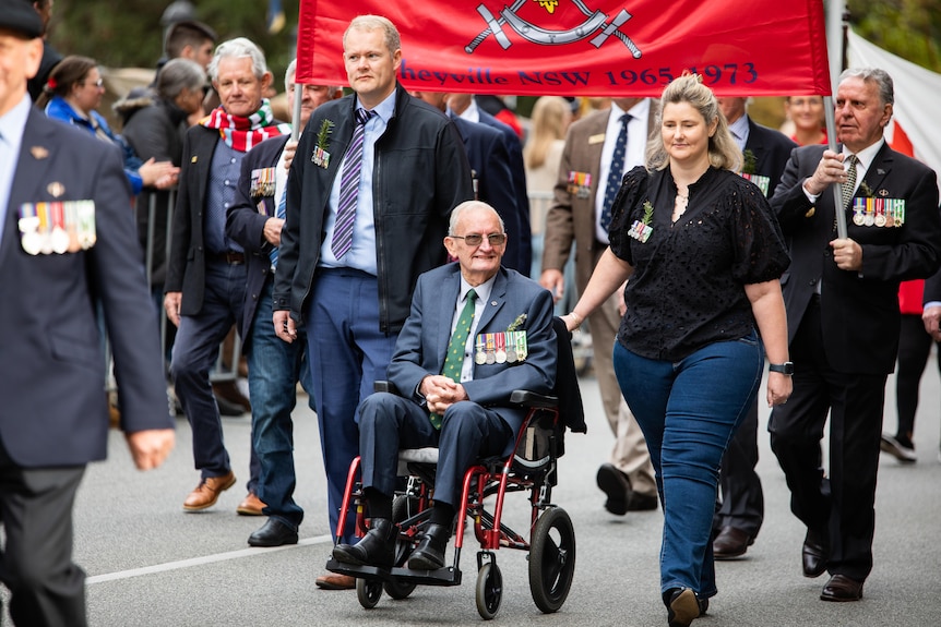 A war veteran in a wheelchair smiles as he is pushed by a man and a woman during an Anzac Day parade in Perth.