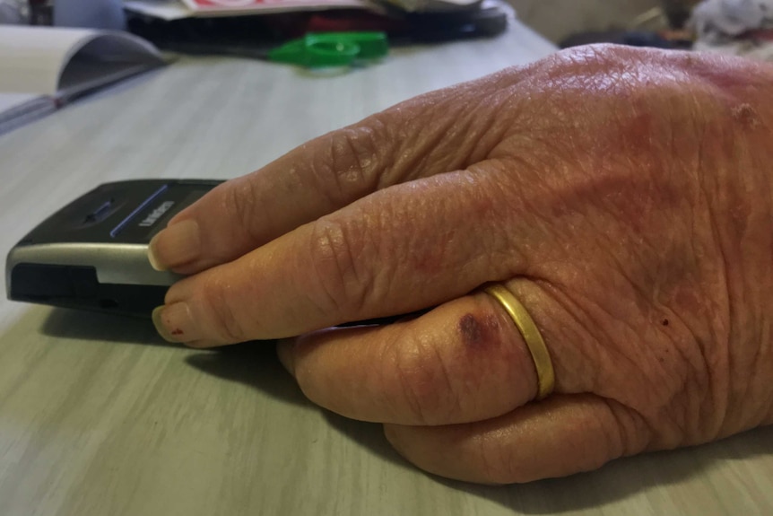 An elderly woman's hand holding a cordless phone on a kitchen table