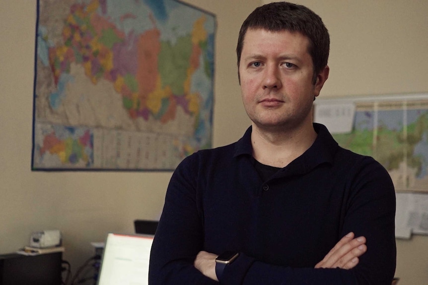 Pollster Denis Volkov stands in an office, frowning with his arms crossed.