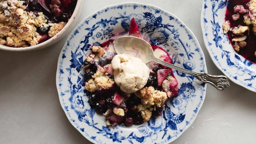 A plate with pear and blueberry crumble and a scoop of ice cream, a quick and easy fruit based dessert.