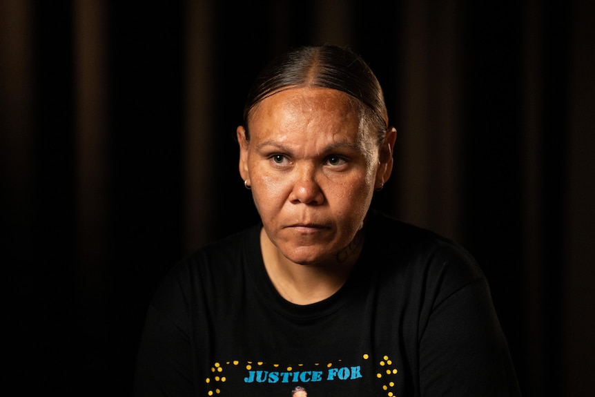 An Indigenous woman looks just past the camera pictured against a black background