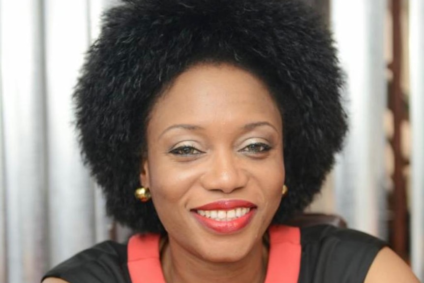 A woman with short dark afro hair smiling wearing a pink and black blouse 
