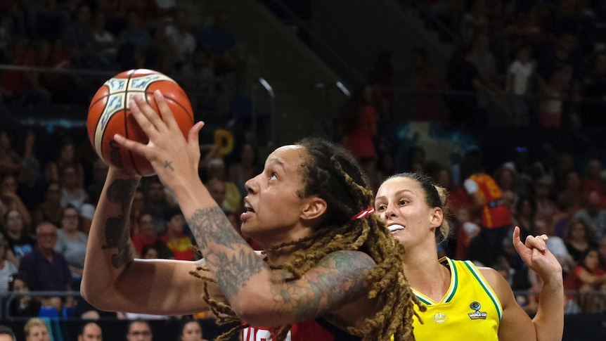 A female basketball players shoots the ball with another player behind her watching on