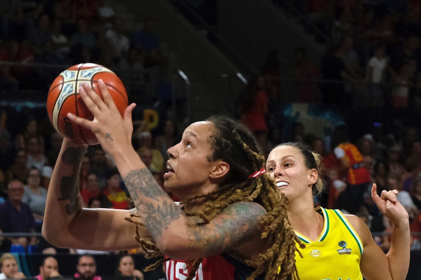 A female basketball players shoots the ball with another player behind her watching on