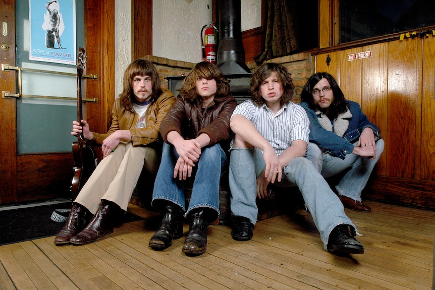 The band Kings of Leon huddle for a portrait against an old fire stove in the corner of a wood-paneled floor