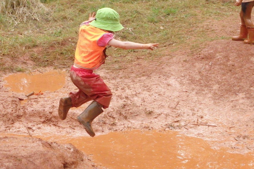 A girl jumps into a muddy puddle during a Nature School session.