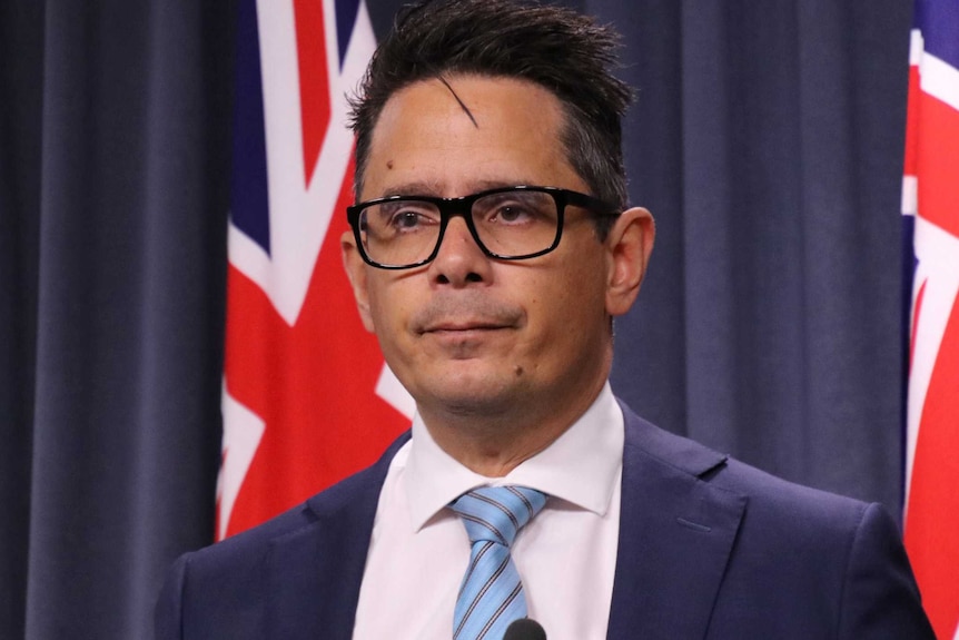 A mid shot of a stern looking WA Treasurer Ben Wyatt standing at a podium in front of two flags.