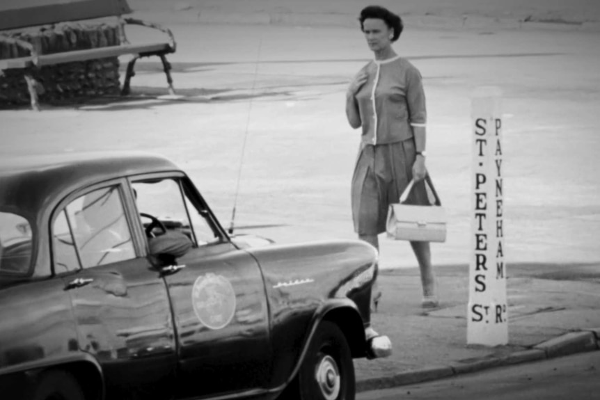 Black and white photo of a well dressed woman walking down a street in Adelaide with a handbag