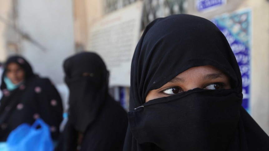 A woman stands in the street wearing a black niaqb peering to her left