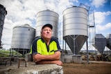 David Williams leans on a concrete block with silos in the background.