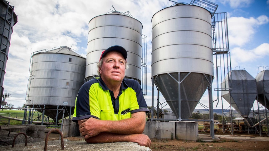 David Williams leans on a concrete block with silos in the background.