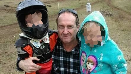 David Routledge kneels with two children on his knee in a bike park.