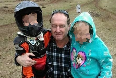 David Routledge kneels with two children on his knee in a bike park.