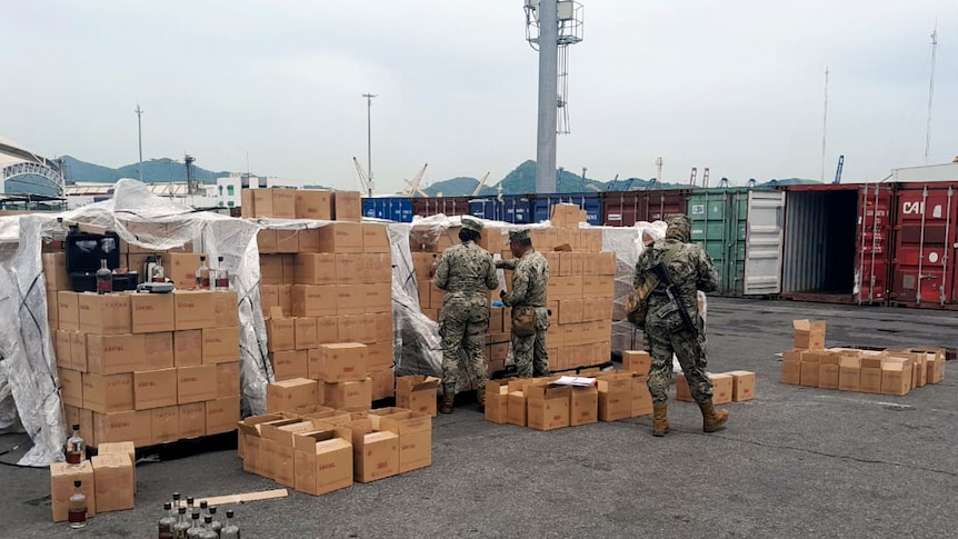 Men in camo uniforms inspect boxes and boxes full of Mezcal bottles