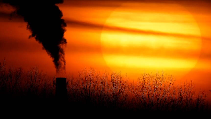 Smoke pours out of a chimney in front of an orange sunset