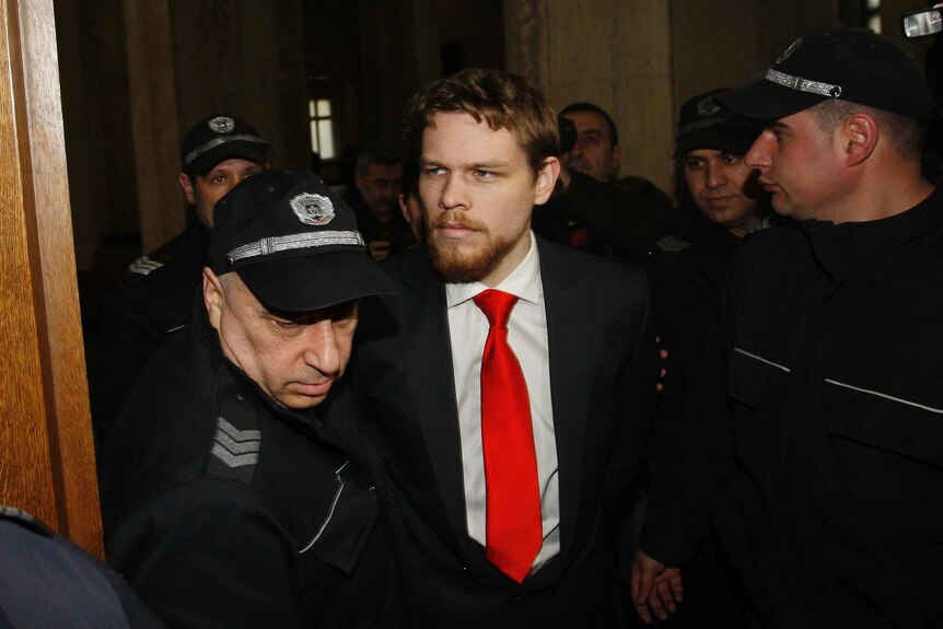 A man in a suit and red tie surrounded by Bulgarian police officers