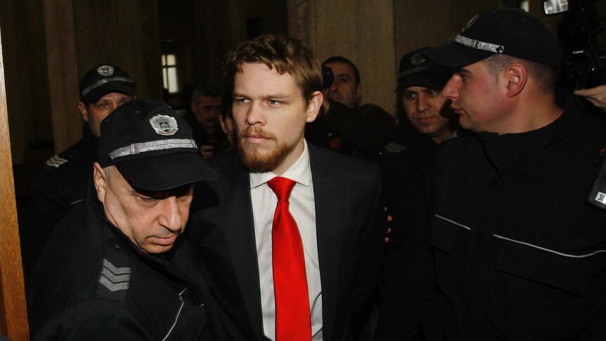 A man in a suit and red tie surrounded by Bulgarian police officers