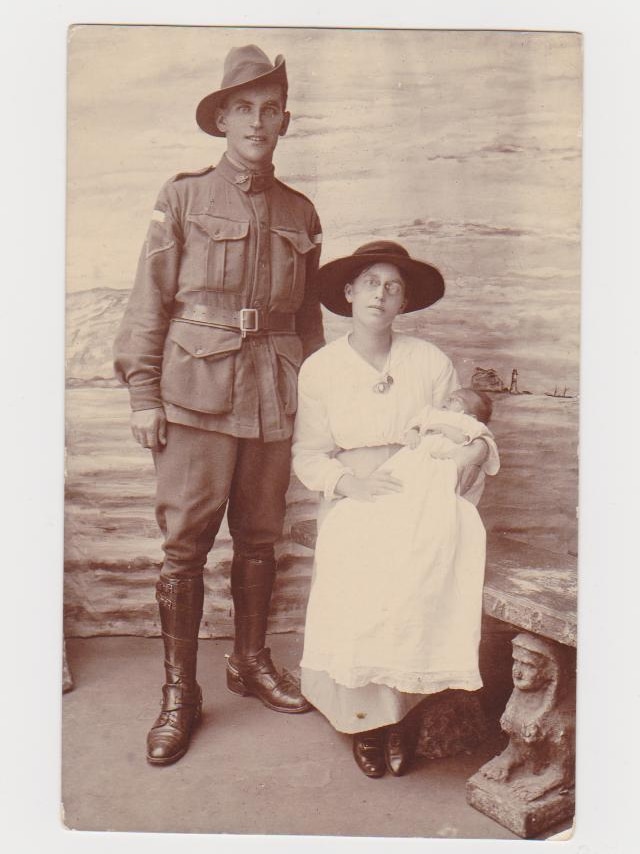 A man in military uniform and slouch hat stands next to a woman wearing a wide hat and dressed in white holding a baby.