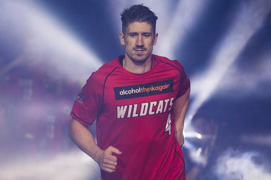 Perth Wildcats forward Greg Hire runs onto court in his red warm-up gear surrounded by strobing lights and smoke.