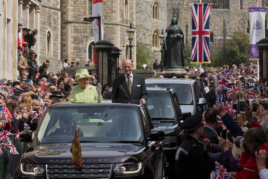 Queen Elizabeth waves from an open-topped car.